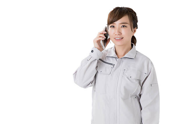 スマートフォンで問い合わせをする若い作業服姿の女性