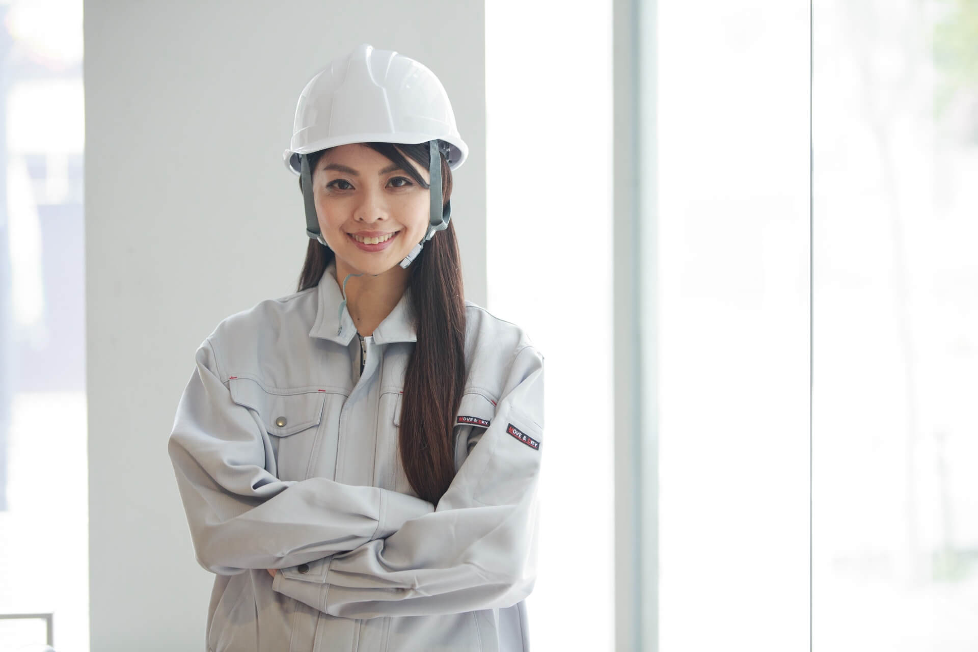 ヘルメットと作業服姿で腕組みをする若い女性従業員